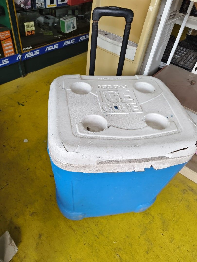 Igloo Ice Cube Rolling Cooler Blue White (Category: Food Organization & Storage) located in Pasig City. Submitted by maming73 (Listing ID 1468306365, Image 1). Description: - Color: Blue and White - Portable design: Telescoping handle and smooth-rolling wheels - Convenience: 4 molded cup holders on the lid - Condition: Fully functional handle and wheels; noticeable scuffs on the body and cracks around the lid edges - Perfect for beach trips, outi