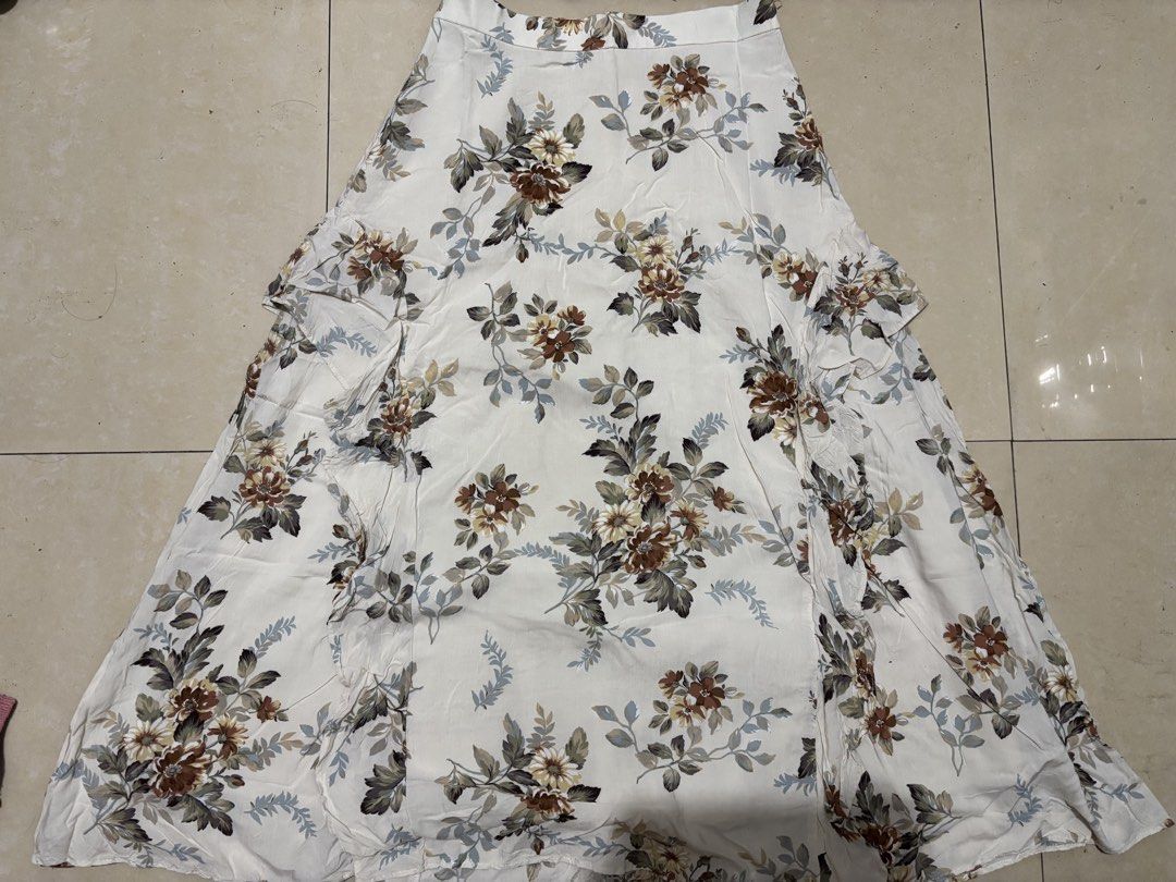 Jill Stuart Floral Long Skirt Size 2 (Category: Skirts) located in Manila. Submitted by van390867 (Listing ID 1468411078, Image 1). Description: - Brand: Jill Stuart Size 25 - Color/Pattern: Cream base with brown, green, and yellow floral print - Size: 2 (tag attached near waistband) - Closure: Side zipper - Details: Ruffled drape down the front, fully lined - Style: Cottagecore / vintage-inspired long skirt.