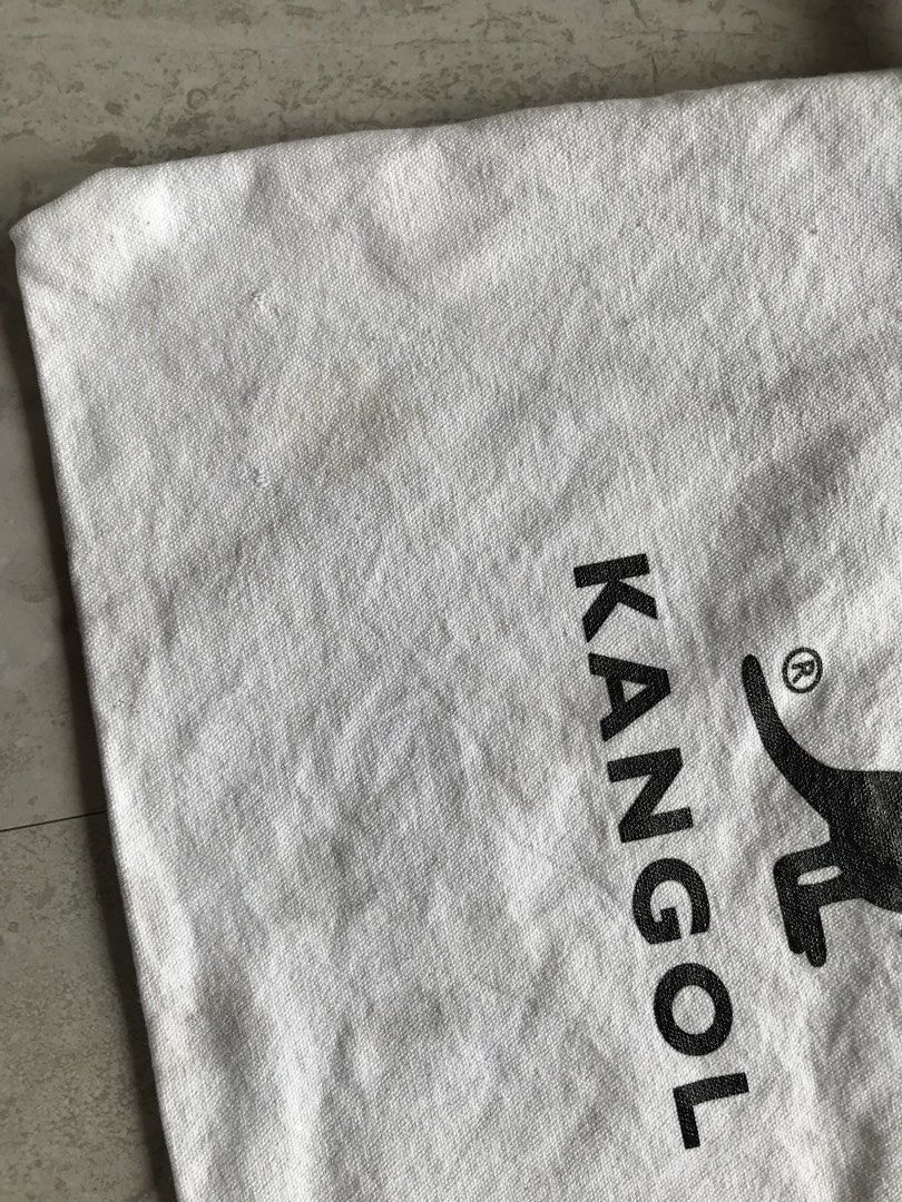 Kangol Canvas Tote Bag KKEB-EB0013F (Category: Tote Bags) located in Banga. Submitted by jorguarino (Listing ID 1468297638, Image 3). Description: Kangol white canvas tote bag with black kangaroo logo graphic on the front. Double carry handles plus longer shoulder straps. 100% cotton material, model KKEB-EB0013F in IV colorway, size OS. Interior has a fabric brand patch sewn onto the pocket. Minor yellowing spots near the bottom left corner..