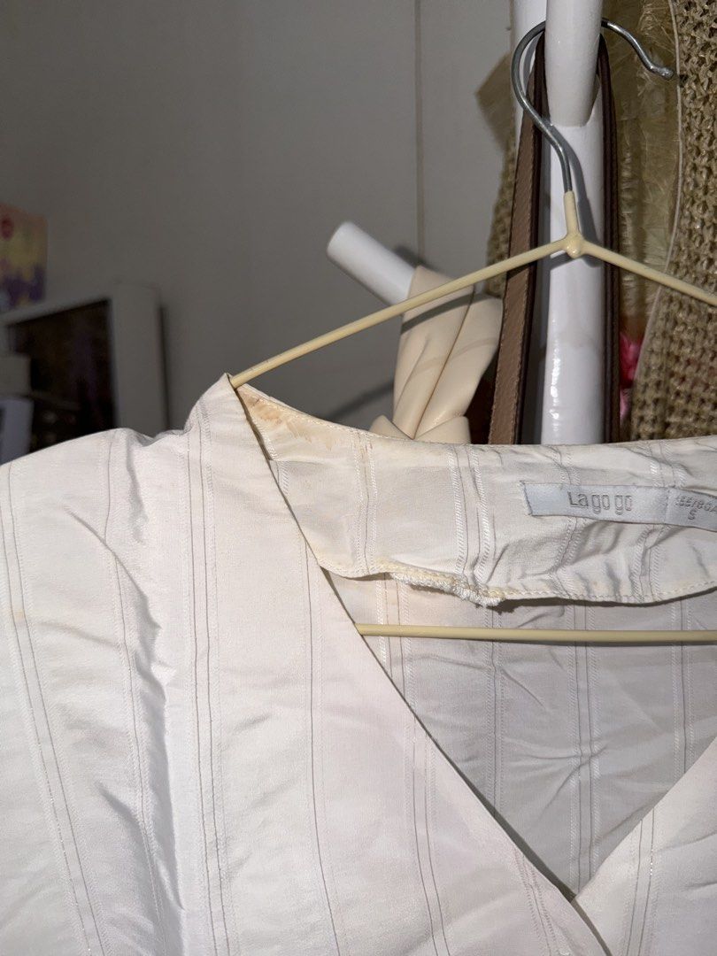 La gogo white striped button-up blouse size S (Category: Blouses) located in Taguig. Submitted by deguzmanke83356 (Listing ID 1468329023, Image 2). Description: - Brand: La gogo - Size: S - Color/Pattern: White with vertical stripes - Style: V-neck, fitted waist, and short sleeves with tie cuffs - Flaws: Visible yellowing stains around the inner collar and a small brown spot on the front right side (can be removed thru hand wash).