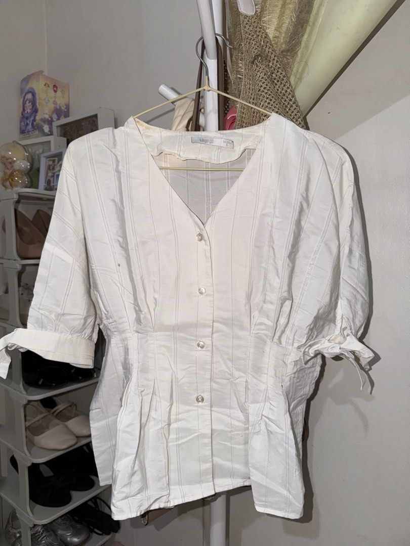 La gogo white striped button-up blouse size S (Category: Blouses) located in Taguig. Submitted by deguzmanke83356 (Listing ID 1468329023, Image 1). Description: - Brand: La gogo - Size: S - Color/Pattern: White with vertical stripes - Style: V-neck, fitted waist, and short sleeves with tie cuffs - Flaws: Visible yellowing stains around the inner collar and a small brown spot on the front right side (can be removed thru hand wash).