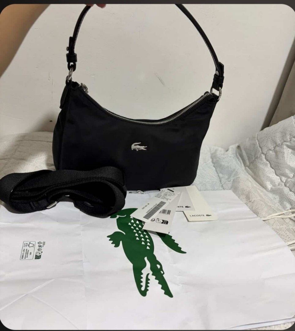 Lacoste Black Nylon Shoulder Bag (Category: Shoulder Bags) located in Polomolok. Submitted by legadad94559 (Listing ID 1468409675, Image 2). Description: - Brand: Lacoste - Color: Classic Black - Material: Lightweight durable nylon with sleek silver hardware - Hardware/Logo: Signature metal crocodile logo on the front - Closure: Secure top zip closure - Straps: Includes a short carry handle and a detachable fabric strap for versatile styling - Co