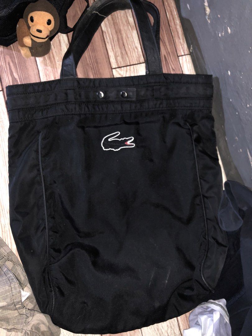 Lacoste Black Tote Bag (Category: Tote Bags) located in Manila. Submitted by fleis.it (Listing ID 1468325376, Image 1). Description: - Brand: Lacoste - Color: Classic Black - Material: Durable nylon fabric - Features: Double top handles, secure snap button closure - Design: Large embroidered crocodile logo on the front - Capacity: Spacious interior, perfect for everyday carry.