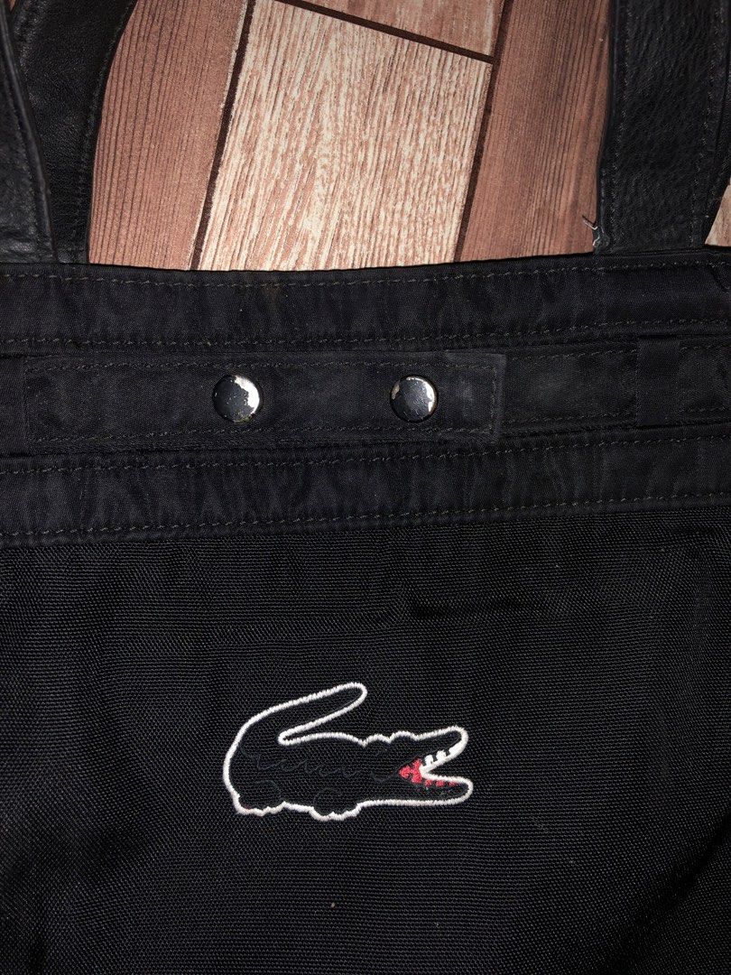 Lacoste Black Tote Bag (Category: Tote Bags) located in Manila. Submitted by fleis.it (Listing ID 1468325376, Image 2). Description: - Brand: Lacoste - Color: Classic Black - Material: Durable nylon fabric - Features: Double top handles, secure snap button closure - Design: Large embroidered crocodile logo on the front - Capacity: Spacious interior, perfect for everyday carry.