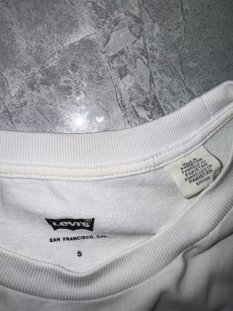 Levi's White Graphic Tee Size S (Category: Tshirts & Polo Shirts ) located in Manila. Submitted by tanlaxfinds (Listing ID 1468321434, Image 3). Description: - Brand: Levi's - Style: White t-shirt with red distressed batwing logo - Size: Small - Material: Soft cotton - Fit: Standard fit with classic crew neck and short sleeves - Origin: Made in Pakistan - Condition: Clean, well-maintained.