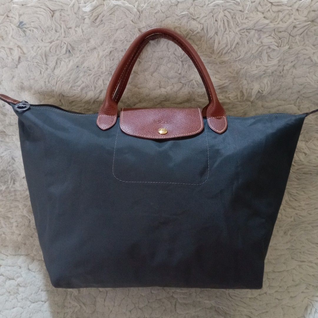 Longchamp Le Pliage Nylon Tote Bag (Category: Luxury Bags & Wallets) located in Baguio. Submitted by sheren_signatures (Listing ID 1468287950, Image 1). Description: - Color & Material: Dark grey nylon body with contrasting brown leather handles and flap - Hardware: Silver-tone zipper pull featuring the iconic horse rider logo and 1948 branding - Closure: Secure top zip closure paired with a front snap button flap featuring a debossed jockey deta