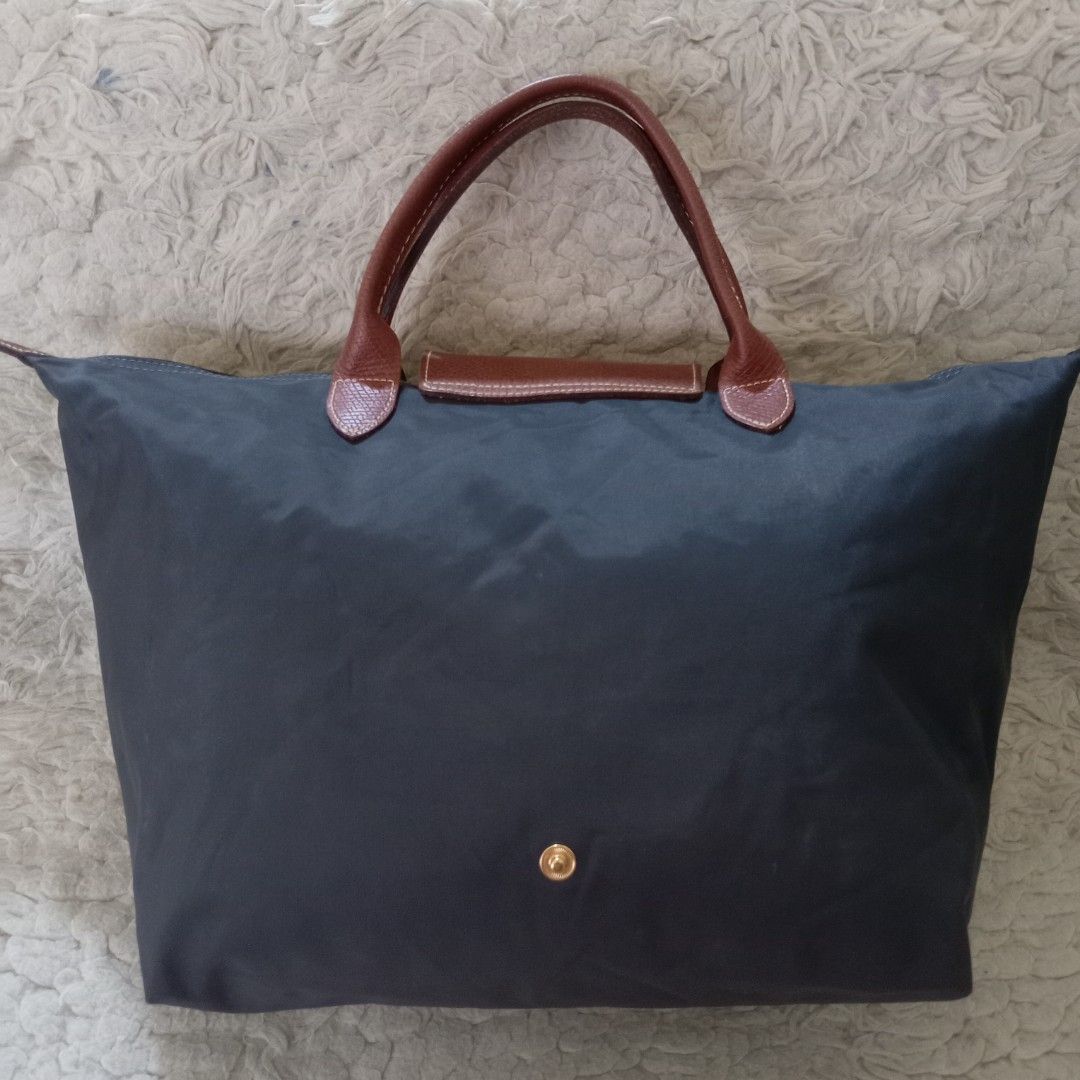 Longchamp Le Pliage Nylon Tote Bag (Category: Luxury Bags & Wallets) located in Baguio. Submitted by sheren_signatures (Listing ID 1468287950, Image 2). Description: - Color & Material: Dark grey nylon body with contrasting brown leather handles and flap - Hardware: Silver-tone zipper pull featuring the iconic horse rider logo and 1948 branding - Closure: Secure top zip closure paired with a front snap button flap featuring a debossed jockey deta