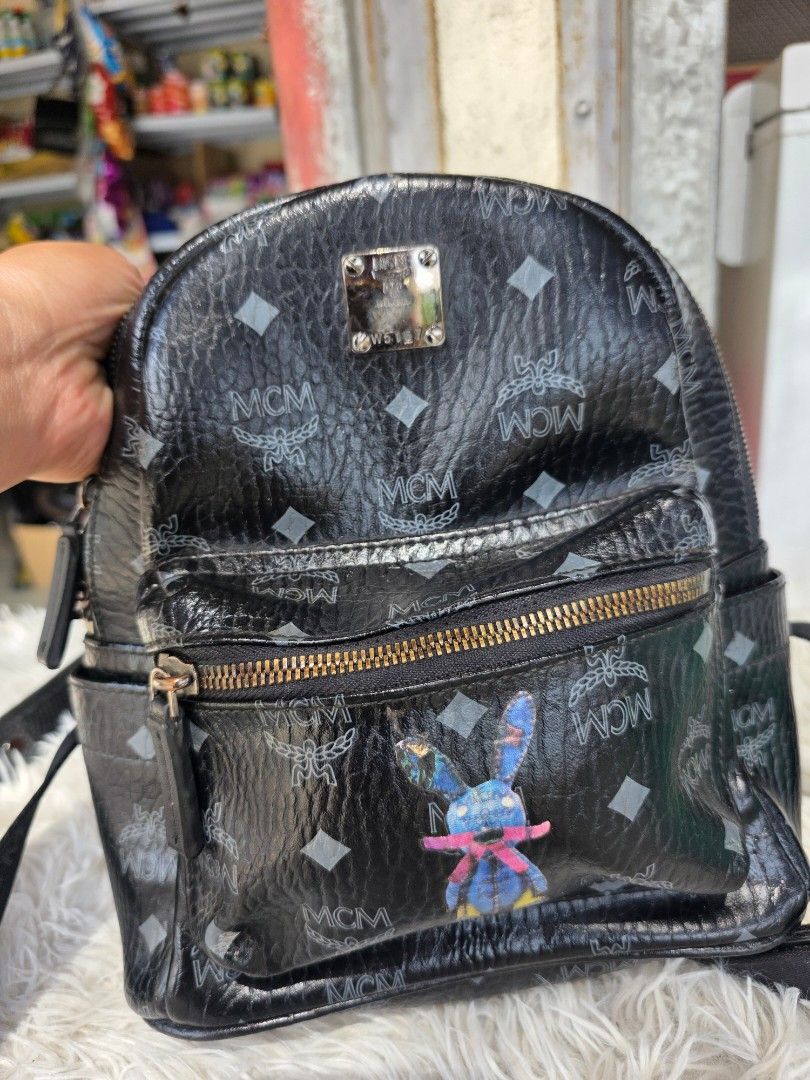 MCM Black Stark Visetos Mini Backpack with Blue Rabbit Patch (Category: Backpacks) located in Lemery. Submitted by venus23 (Listing ID 1468306236, Image 2). Description: - Brand: MCM Mini Backpack - Color: Black with grey monogram print - Design: Front zipped pocket with a blue rabbit graphic patch - Hardware: Silver-tone with metal logo plaque - Features: Adjustable shoulder straps, top handle, durable coated canvas - Condition: Minor scratches 
