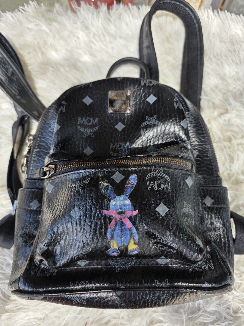 MCM Black Stark Visetos Mini Backpack with Blue Rabbit Patch (Category: Backpacks) located in Lemery. Submitted by venus23 (Listing ID 1468306236, Image 3). Description: - Brand: MCM Mini Backpack - Color: Black with grey monogram print - Design: Front zipped pocket with a blue rabbit graphic patch - Hardware: Silver-tone with metal logo plaque - Features: Adjustable shoulder straps, top handle, durable coated canvas - Condition: Minor scratches 
