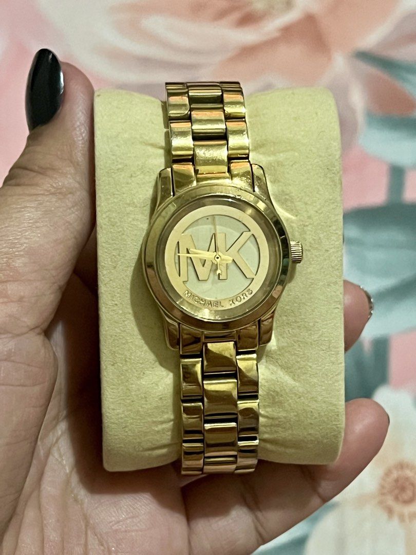 Michael Kors Gold Watch with MK Logo Dial (Category: Women's Watches) located in Dagupan City. Submitted by casadebayongph (Listing ID 1468327367, Image 3). Description: - Brand: Michael Kors - Color: Polished gold-tone finish - Design: Statement watch with large MK logo on the face - Closure: Link bracelet with branded deployment clasp - Condition: Good pre-loved condition with minor hairline scratches on links from normal wear - Style: Elegant,