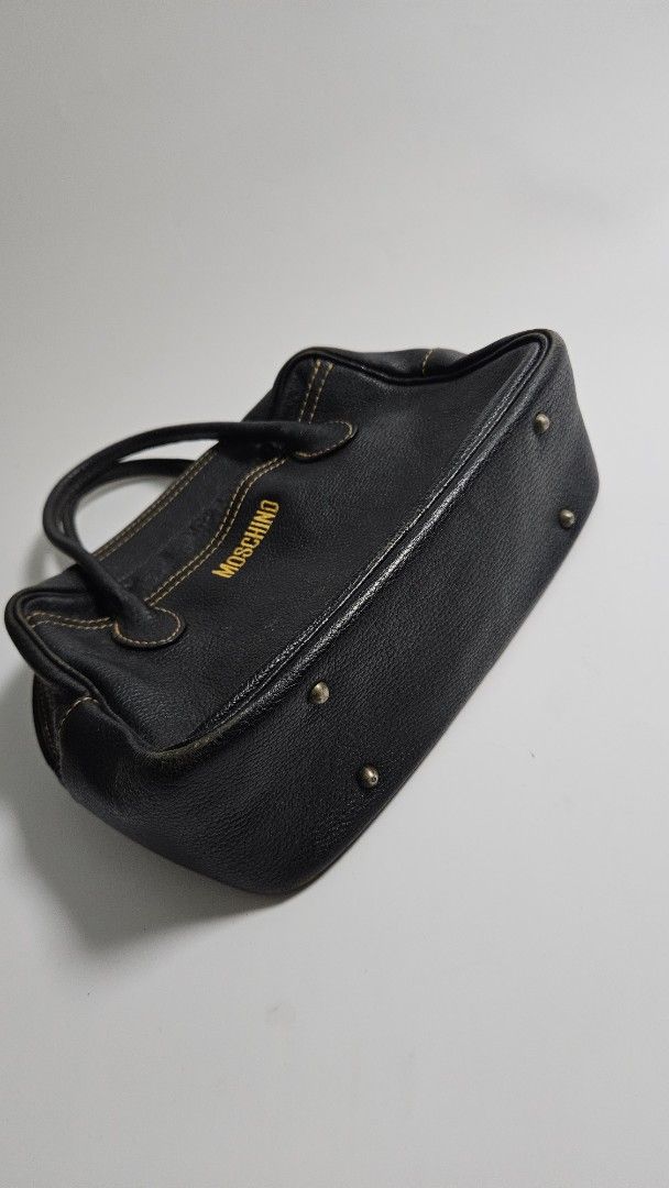 Moschino Black Leather Handbag (Category: Luxury Bags & Wallets) located in Alfonso. Submitted by jbcamet (Listing ID 1468389444, Image 3). Description: - Brand: Moschino - Material: Black pebble leather with fabric lining - Details: Yellow embroidered front logo, contrasting orange stitching - Hardware: Protective metal feet at the base - Closure: Top zip closure with double top handles - Condition: Classic vintage piece with subtle wear - Size: