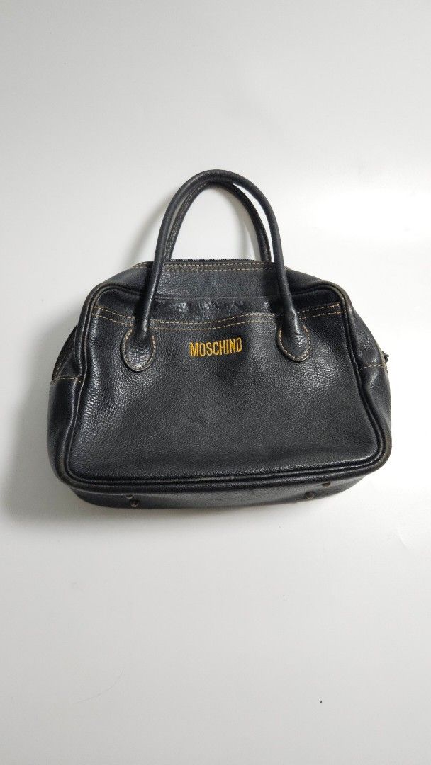 Moschino Black Leather Handbag (Category: Luxury Bags & Wallets) located in Alfonso. Submitted by jbcamet (Listing ID 1468389444, Image 1). Description: - Brand: Moschino - Material: Black pebble leather with fabric lining - Details: Yellow embroidered front logo, contrasting orange stitching - Hardware: Protective metal feet at the base - Closure: Top zip closure with double top handles - Condition: Classic vintage piece with subtle wear - Size: