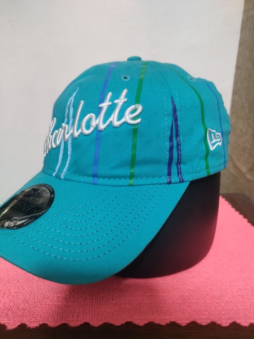 New Era Charlotte Hornets 9TWENTY Adjustable Cap (Category: Caps & Hats) located in Santa Rosa. Submitted by abj_104 (Listing ID 1468304860, Image 3). Description: - Authentic New Era 9TWENTY Cap in Teal - Features embroidered Charlotte script on the front - Unique striped vertical pattern on the crown - Rare NBA 75th anniversary tag on the side - Adjustable strapback closure with a silver metal buckle - with original visor sticker still attached