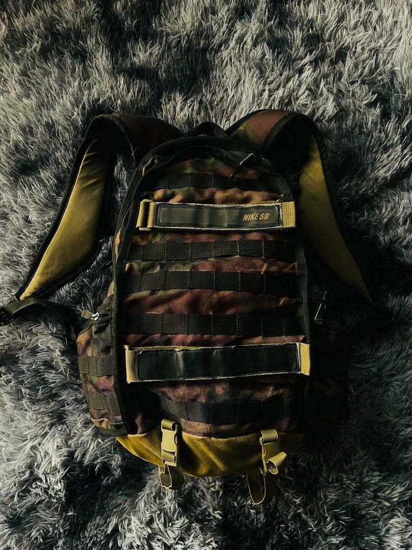 Nike SB Camo Backpack (Category: Backpacks) located in Manila. Submitted by thrift_ni_pambiii (Listing ID 1468344467, Image 1). Description: - Brand: Nike SB - Pattern: Camo with olive green interior lining - Features: Multiple secure zip compartments, heavy-duty front straps, and a front chest buckle strap - Condition: Noticeable tears and fabric damage near the lower back panel area - Best for: Skateboarding, daily commutes, or casual use.