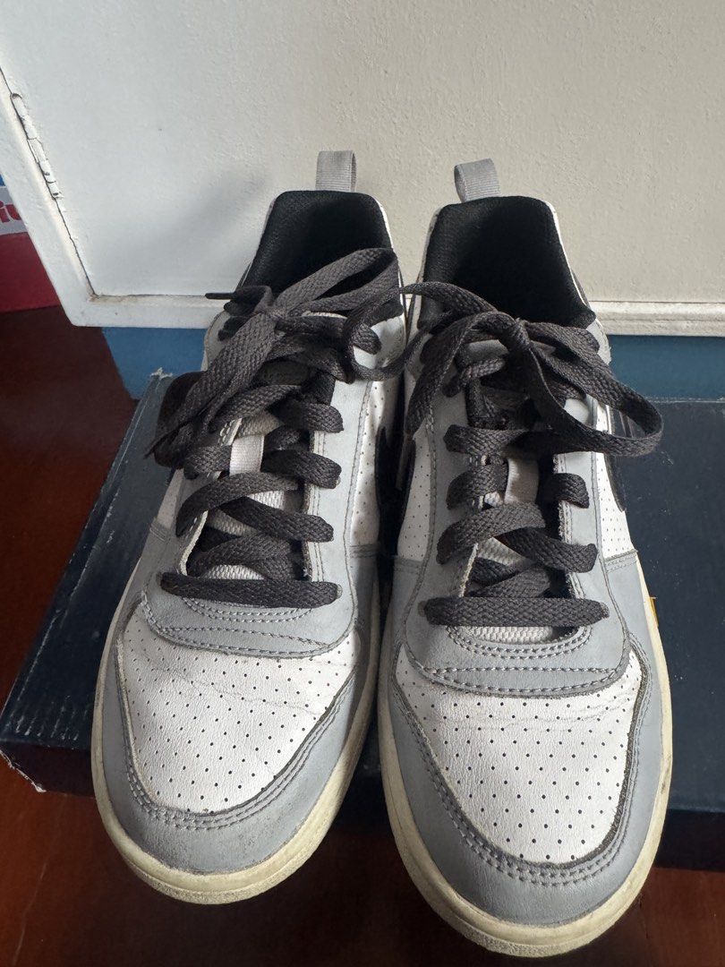 Nike White and Grey Sneakers (Category: Babies & Kids Fashion) located in Batangas. Submitted by GDW98 (Listing ID 1468356187, Image 3). Description: - Brand: Nike - Style: Low-top sneakers - Colorway: White and grey with a black swoosh - Material: Perforated leather upper - Details: Dark grey laces, black inner lining, and grey heel pull tabs - Sole: White rubber soles - Condition: Shows some wear on the midsoles .