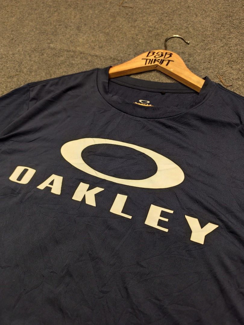 Oakley Performance Fit T-Shirt (Category: Activewear) located in Cordova. Submitted by bsb.streetluxvintage.clothing (Listing ID 1468425204, Image 2). Description: - Brand: Oakley - Color: Navy Blue - Design: Large white Oakley Ellipse logo on chest - Fit/Style: Performance fit - Material: 88% Polyester, 12% Elastane - Size: US/EU Small (JPN Medium) - Condition/Care: Made in China, machine washable.