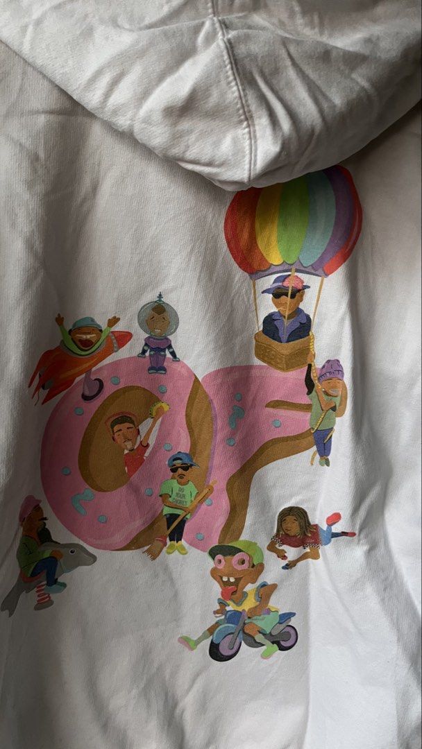 Odd Future Donut White Hoodie Size M (Category: Hoodies) located in Cabuyao City. Submitted by bulandos (Listing ID 1468379631, Image 3). Description: White Odd Future hoodie with the pink donut logo on the chest. Large graphic print on the back featuring cartoon characters around the donut, plus 'Odd Future' text down the left sleeve. Kangaroo pocket in front, drawstring hood. Size medium tag printed inside the collar. 80% cotton, 20% polyester 