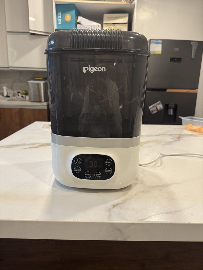 Pigeon Sterilizer with Dryer (Category: Breastfeeding & Bottle Feeding) located in Makati City. Submitted by ckrealty (Listing ID 1468311151, Image 1). Description: - Brand: Pigeon - Features: Digital touch control panel with sterilize, dry, and purify cycles - Design: Dark grey transparent cover lid with internal rack pegs for bottles and accessories - Color: White base with attached power cord - Original Retail Price: ~8,999.75 PHP - Condition:
