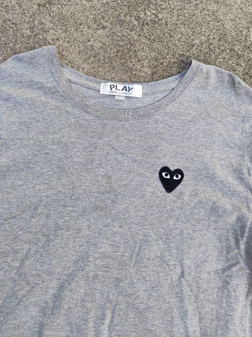 Play Comme des Garcons Grey T-Shirt (Category: Tshirts & Polo Shirts ) located in Lemery. Submitted by dailythriftin (Listing ID 1468435312, Image 3). Description: - Brand: Play Comme des Garcons - Color: Grey - Style: Short sleeve crew neck t-shirt - Details: Signature small black heart patch on chest, large black graphic print near bottom hem - Condition: Excellent, well-maintained - Fit/Vibe: Casual streetwear staple, easy to style with jeans 