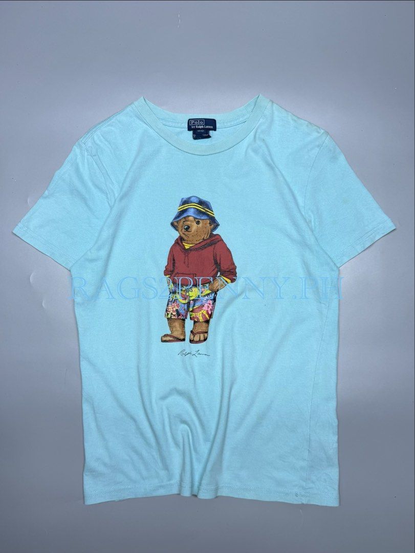 Polo by Ralph Lauren Bear (Category: Tshirts & Polo Shirts ) located in Kabacan. Submitted by rags2penny.phl (Listing ID 1468333222, Image 1). Description: - Brand: Polo by Ralph Lauren - Color: Light Blue - Design: Iconic bear graphic wearing a bucket hat and floral shorts - Details: Short sleeves, crew neck - Size: M(10) - Material: 100% Cotton - Origin: Made in Guatemala - Condition: Excellent pre-loved condition (ready to wear) Measurements :