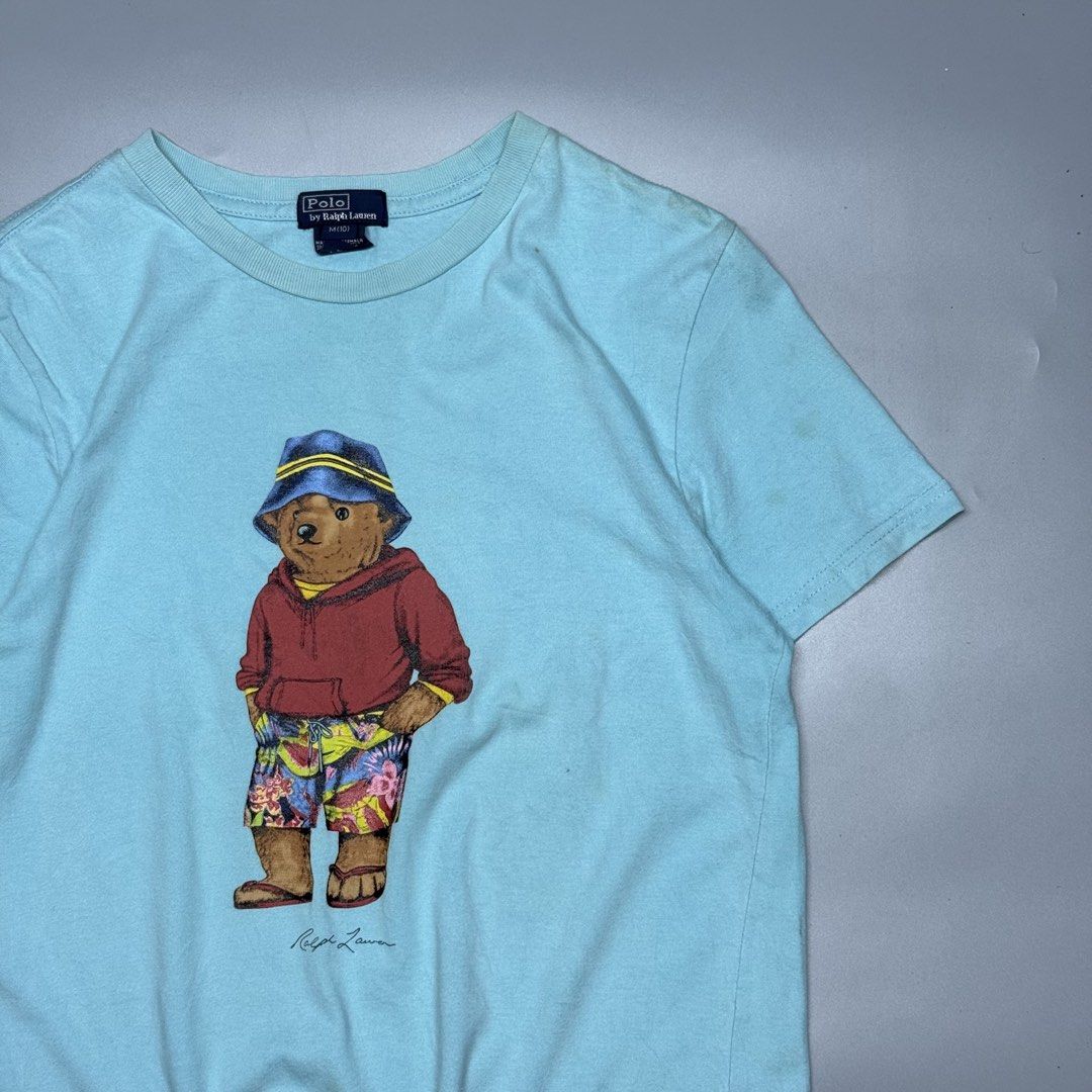 Polo by Ralph Lauren Bear (Category: Tshirts & Polo Shirts ) located in Kabacan. Submitted by rags2penny.phl (Listing ID 1468333222, Image 2). Description: - Brand: Polo by Ralph Lauren - Color: Light Blue - Design: Iconic bear graphic wearing a bucket hat and floral shorts - Details: Short sleeves, crew neck - Size: M(10) - Material: 100% Cotton - Origin: Made in Guatemala - Condition: Excellent pre-loved condition (ready to wear) Measurements :