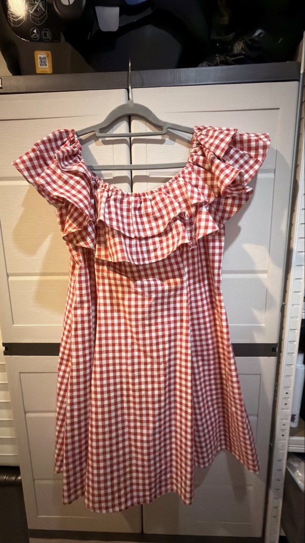 Red and White Gingham Off-Shoulder Dress (Category: Dresses) located in Manila. Submitted by adoptmypreloveditems (Listing ID 1468476465, Image 1). Description: - Design: Red and white check pattern with off-shoulder cut - Details: Layered ruffle neckline and sleeves - Fit: Short flared cut, clean overall shape - Material: Lightweight and breathable fabric - Condition: Excellent, ready to wear for sunny days.