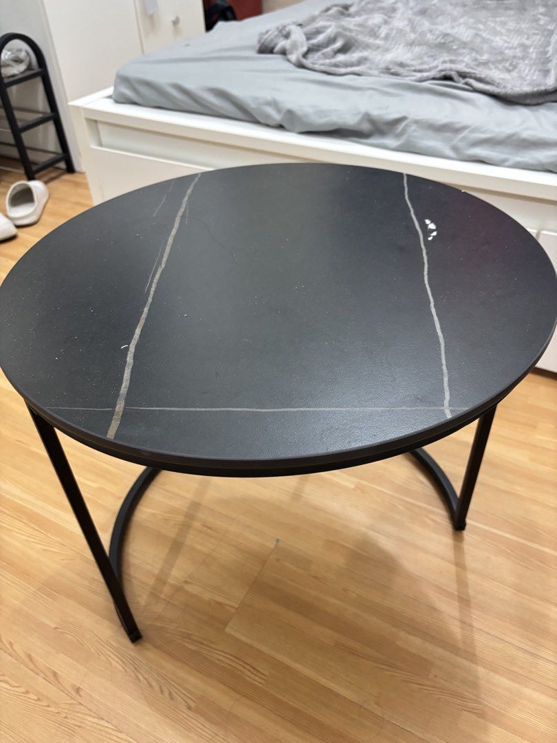 Round Black Coffee Table with Metal Frame (Category: Tables & Sets) located in Cavite. Submitted by xxjxt (Listing ID 1468403904, Image 2). Description: - Type: Round coffee table - Dimensions: Approx. 1 meter across - Materials: Dark stone-pattern top with sturdy black metal base and semi-circular legs - Condition: Noticeable surface wear, light scratches, water rings, and minor paint chipping near the edge; structurally solid - Ideal for: Livin