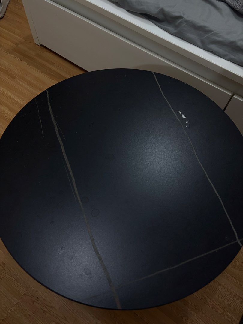 Round Black Coffee Table with Metal Frame (Category: Tables & Sets) located in Cavite. Submitted by xxjxt (Listing ID 1468403904, Image 3). Description: - Type: Round coffee table - Dimensions: Approx. 1 meter across - Materials: Dark stone-pattern top with sturdy black metal base and semi-circular legs - Condition: Noticeable surface wear, light scratches, water rings, and minor paint chipping near the edge; structurally solid - Ideal for: Livin