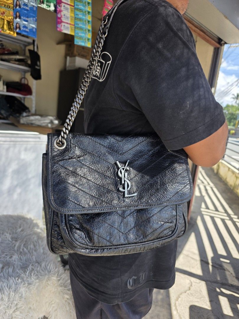 Saint Laurent Black Leather Chain Bag (Category: Shoulder Bags) located in Lemery. Submitted by venus23 (Listing ID 1468306614, Image 1). Description: Black crinkled leather shoulder bag from Saint Laurent. Features quilted chevron pattern and silver-tone hardware. YSL monogram logo on the front flap. Chain strap with leather shoulder guard. Magnetic snap closure engraved with Saint Laurent Paris branding. Metal grommets with etched brand text..