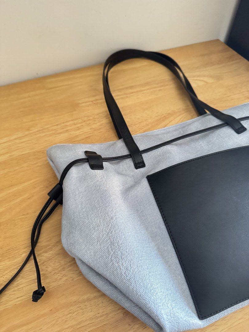 Sanfu Grey and Black Tote Bag (Category: Tote Bags) located in Mandaluyong City. Submitted by uol77 (Listing ID 1468306725, Image 2). Description: - Brand: Sanfu - Color: Grey textured body with black leather handles and front pocket - Design: Black drawstring accent along the top edge - Interior: White fabric lining featuring a zipped pocket and Sanfu brand patch - Condition: Pre-loved with some dirt stains inside the lining and a minor mark on 