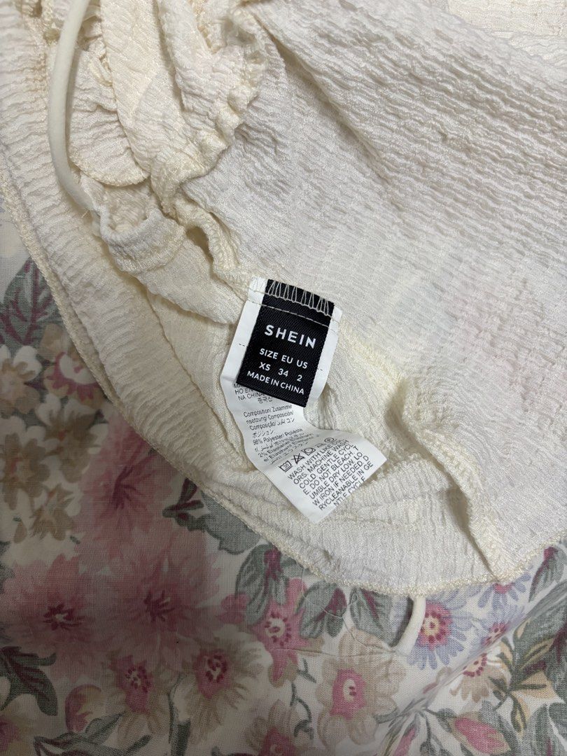 SHEIN White Ruffle Camisole Size XS (Category: Sleeveless) located in Manila. Submitted by urthrifthany (Listing ID 1468443130, Image 2). Description: - Brand: SHEIN - Size: XS - Color: White with subtle texture - Material: 98% polyester, 2% elastane (lightweight & comfy) - Features: Thin spaghetti straps, sweet ruffled neckline, flowy peplum hem - Condition: Great, perfect for sunny weather or casual styling.
