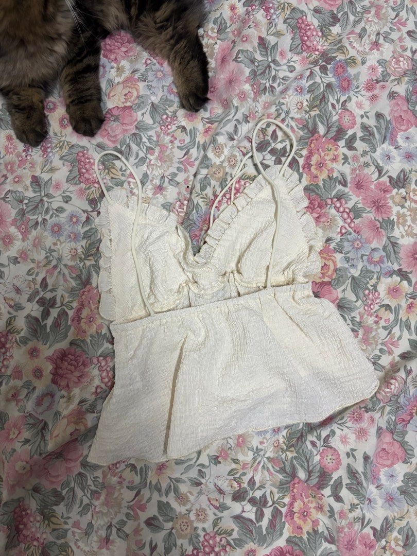 SHEIN White Ruffle Camisole Size XS (Category: Sleeveless) located in Manila. Submitted by urthrifthany (Listing ID 1468443130, Image 1). Description: - Brand: SHEIN - Size: XS - Color: White with subtle texture - Material: 98% polyester, 2% elastane (lightweight & comfy) - Features: Thin spaghetti straps, sweet ruffled neckline, flowy peplum hem - Condition: Great, perfect for sunny weather or casual styling.