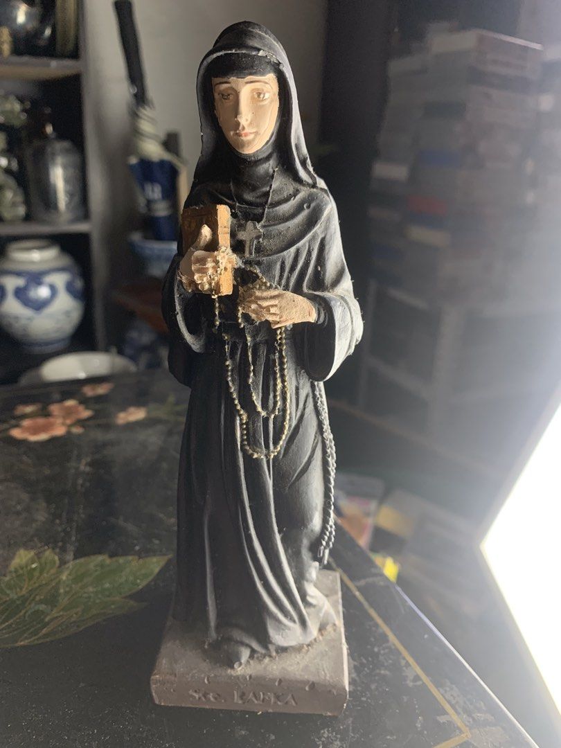 St. Rafka statue nun figurine religious decor (Category: Religious Items) located in Quezon City. Submitted by sojisup (Listing ID 1468325649, Image 2). Description: - Item: St. Rafka Nun Figurine - Appearance: Dressed in a grey habit and veil - Details: Holds a small wooden book and rosary beads - Base: Inscribed with 'Ste. RAFKA' - Condition: Pre-owned display item with some dust accumulation.