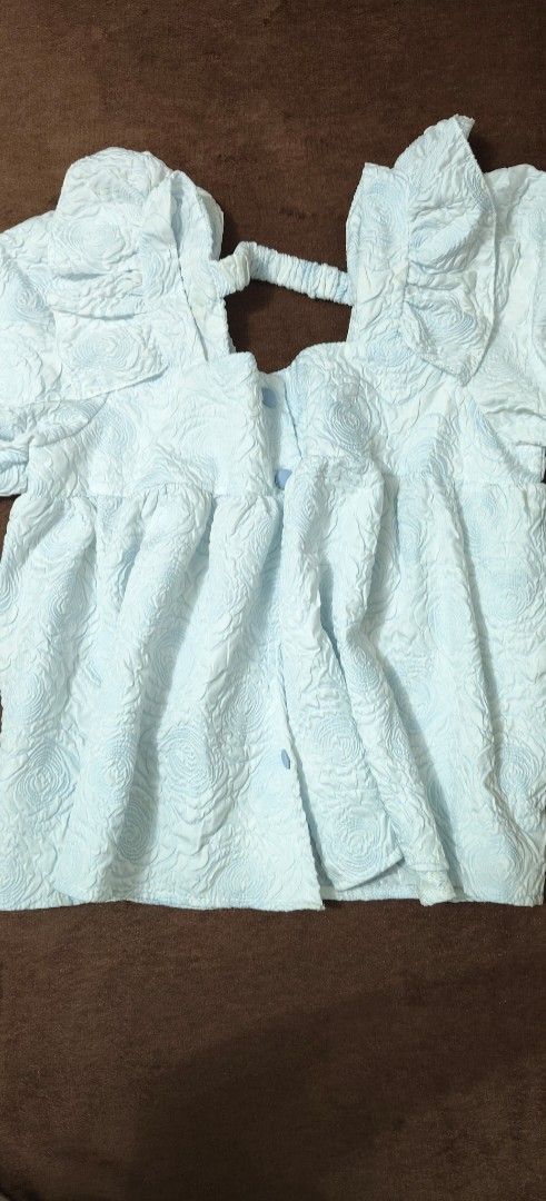 Three Princess Blue Textured Floral Blouse (Category: Blouses) located in Manila. Submitted by snz_shop (Listing ID 1468472570, Image 1). Description: - Brand: Three Princess - Color: Light Blue - Style: Short-sleeve peplum top with button front - Details: All-over textured floral pattern, ruffle shoulders, and elasticized back strap - Fabric: Lightweight and airy, perfect for warm weather - Condition: Excellent.
