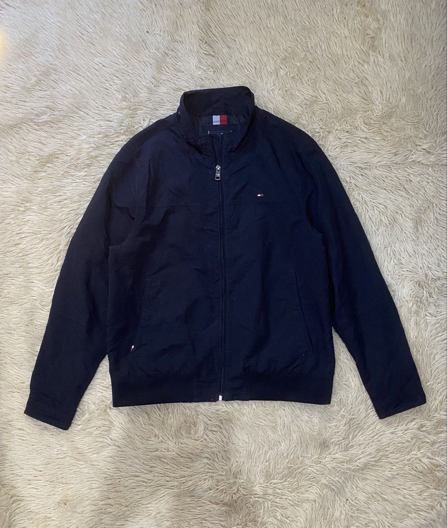 Tommy Hilfiger Navy Blue Zip-Up Jacket Size L (Category: Coats, Jackets and Outerwear) located in Manila. Submitted by switchcity (Listing ID 1468431013, Image 1). Description: - Brand: Tommy Hilfiger - Color: Navy Blue - Size: L (180/108B) - Material: 100% Nylon shell with polyester lining - Design: High collar with bold back branding, full front zipper, side pockets, and buttoned cuffs - Logo: Classic Tommy flag logo embroidered on the chest - 