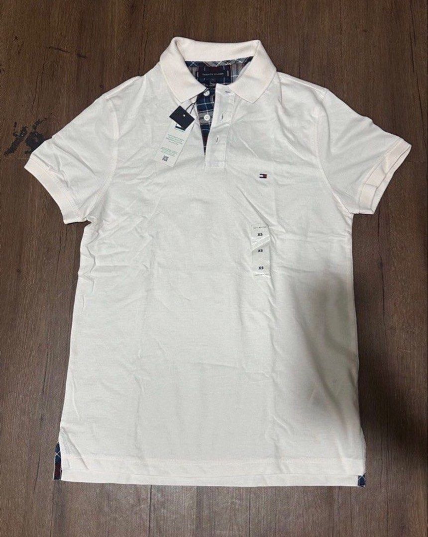 Tommy Hilfiger White Polo Shirt (Category: Tshirts & Polo Shirts ) located in Subic. Submitted by declutterbyshit (Listing ID 1468357912, Image 1). Description: - Brand: Tommy Hilfiger - Item: White Polo Shirt - Size: XS on tag but fits s-m (28x19) - Condition: Brand new, never worn, with original store tags and plastic size strips attached - Details: Classic collar with blue plaid inner lining and placket trim - Branding: Small embroidered logo 