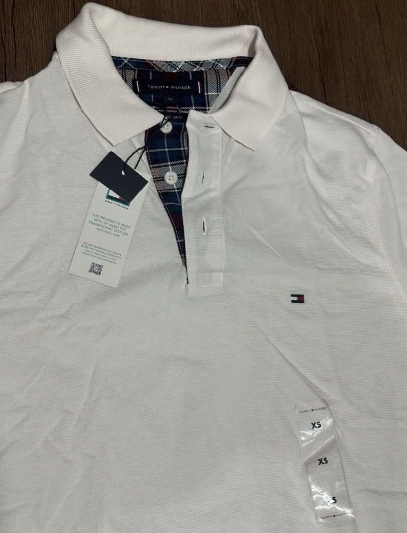 Tommy Hilfiger White Polo Shirt (Category: Tshirts & Polo Shirts ) located in Subic. Submitted by declutterbyshit (Listing ID 1468357912, Image 2). Description: - Brand: Tommy Hilfiger - Item: White Polo Shirt - Size: XS on tag but fits s-m (28x19) - Condition: Brand new, never worn, with original store tags and plastic size strips attached - Details: Classic collar with blue plaid inner lining and placket trim - Branding: Small embroidered logo 