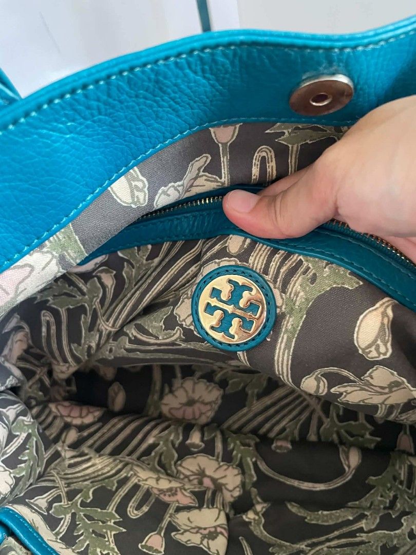 Tory Burch Teal Pebbled Leather Tote Bag (Category: Tote Bags) located in Digos. Submitted by chicandglowbargains (Listing ID 1468070858, Image 3). Description: - Brand: Tory Burch - Material: Premium teal pebbled leather - Hardware: Gold-tone double-T logo on front - Straps: Comfortable double shoulder straps with structured drop - Interior: Spacious with a decorative floral and vine pattern, plus an interior zip pocket - Base: Structured base p