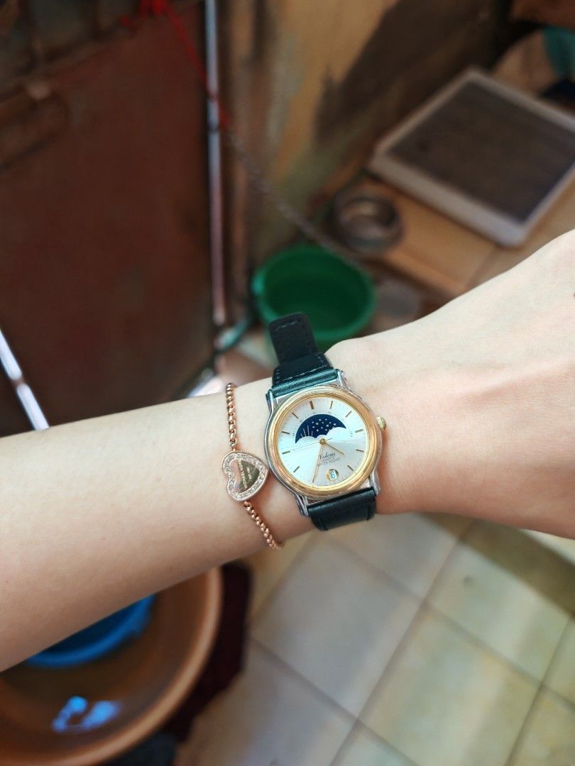 Volcas Quartz Watch Moon Phase Dial Black Leather Strap (Category: Women's Watches) located in Taguig. Submitted by mystuff4youph (Listing ID 1468364501, Image 2). Description: - Brand/Model: Volcas Quartz Watch - Dial: Silver sunburst face with unique moon phase dial and date window at the bottom - Movement: Reliable Japan movement - Design: Gold-toned bezel with stainless steel case back and clean glass - Strap: Black leather strap with a stand