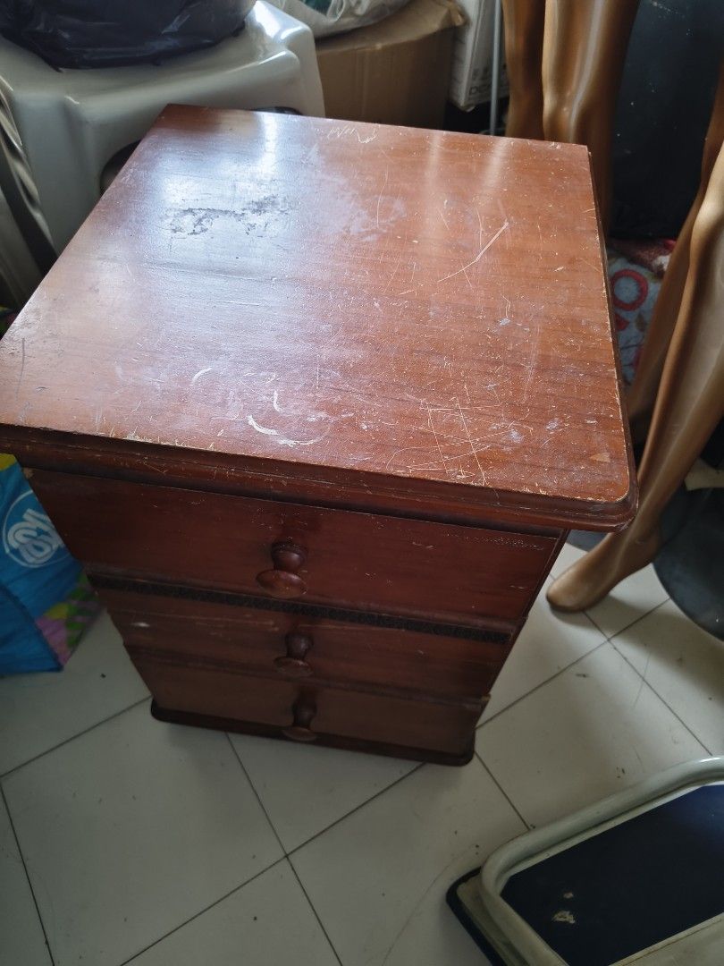 Wooden Bedside Table with 3 Drawers (Category: Shelves, Cabinets & Racks) located in Pasig City. Submitted by maming73 (Listing ID 1468306178, Image 2). Description: - Material: Solid wooden bedside table with a medium brown finish - Storage: 3 spacious drawers featuring round wooden knobs and a decorative dark trim - Design: Sturdy freestanding unit with solid feet - Condition: Shows visible wear, scratches, and scuffs on the top surface and dra