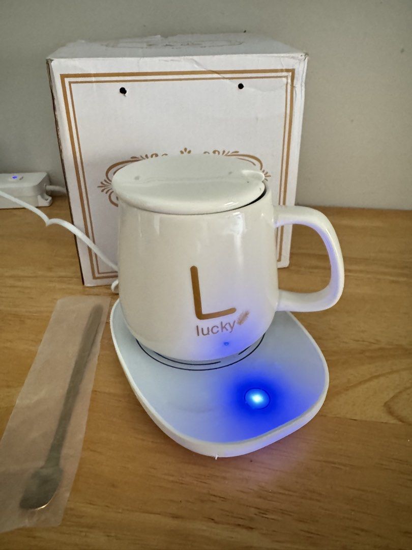 Y2 Coffee Cup and Saucer Mug Warmer Set (Category: Coffee & Tea Tableware) located in Mandaluyong City. Submitted by uol77 (Listing ID 1468302136, Image 2). Description: Y2 brand smart coffee cup warmer set. Includes white ceramic mug with letter L and lucky text, matching lid, warming coaster plate, golden spoon, and original box. Keeps drinks warm while working at the desk. Plug-in electric warmer base lights up blue when turned on. Everything 