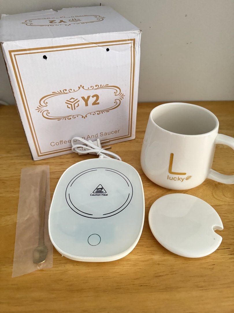 Y2 Coffee Cup and Saucer Mug Warmer Set (Category: Coffee & Tea Tableware) located in Mandaluyong City. Submitted by uol77 (Listing ID 1468302136, Image 3). Description: Y2 brand smart coffee cup warmer set. Includes white ceramic mug with letter L and lucky text, matching lid, warming coaster plate, golden spoon, and original box. Keeps drinks warm while working at the desk. Plug-in electric warmer base lights up blue when turned on. Everything 