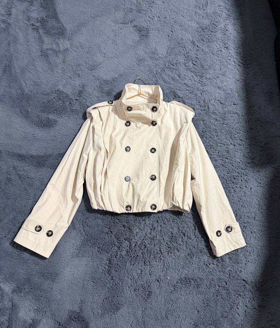 Zara Beige Cropped Trench Coat (Category: Coats, Jackets and Outerwear) located in Las Pinas. Submitted by juls_mp (Listing ID 1468428276, Image 1). Description: - Color: Cream - Style: Cropped jacket with gathered elastic waist - Material: Lightweight cotton fabric - Details: Double-breasted tortoise shell buttons - Neckline: High standing collar - Accents: Shoulder epaulets and button tabs on wide cuffs - Condition: Brand new, removed tag only 