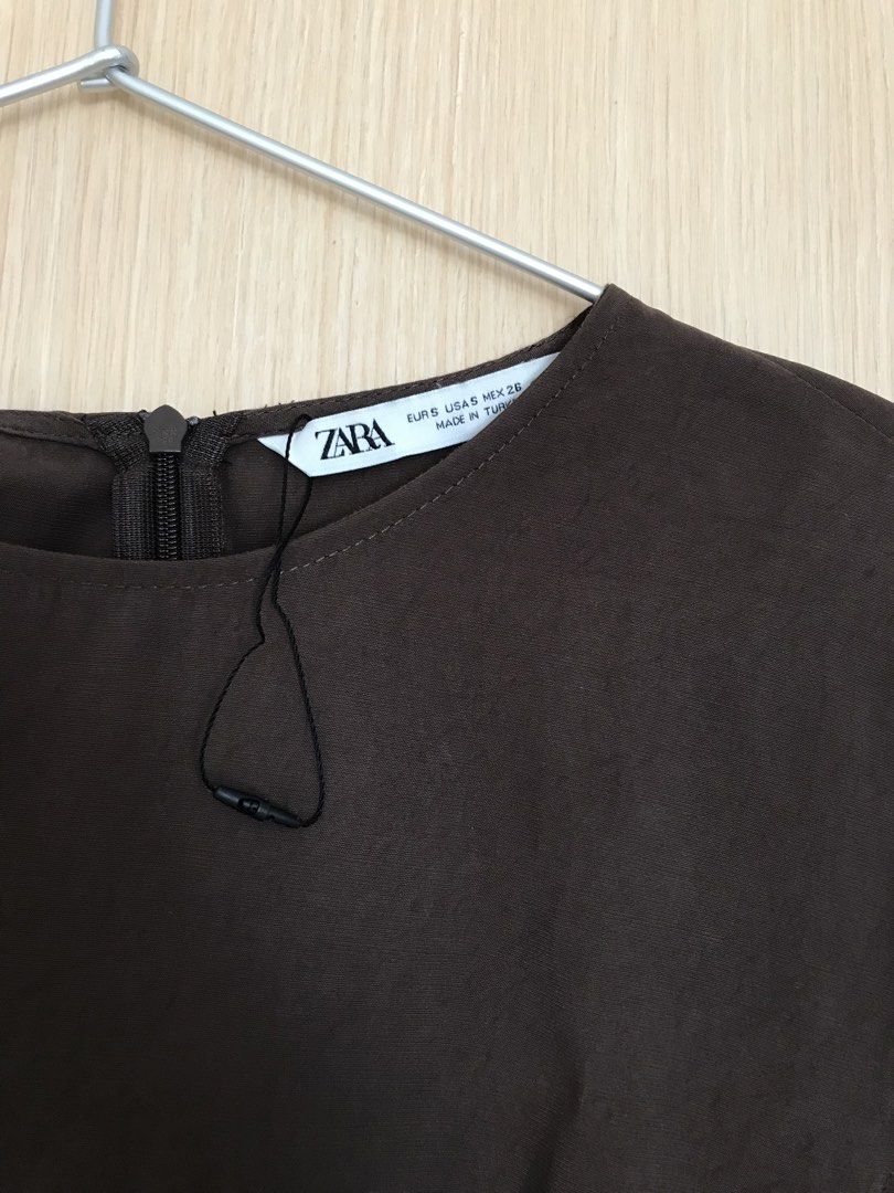 ZARA Dark Brown Blouse Size S (Category: Blouses) located in Cainta. Submitted by ukaymama (Listing ID 1468295786, Image 2). Description: - Brand: ZARA - Size: S - Color: Dark Brown - Material/Origin: Made in Turkey - Design: Short sleeves, round neckline, back zipper closure, and a unique front draped panel - Condition: Excellent, clean with no stains or damage.