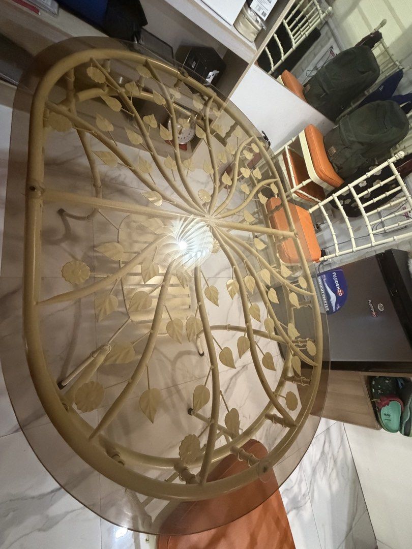 4 seater glass top dining set (Category: Tables & Sets) located in Manila. Submitted by noblebird-f4dd (Listing ID 1468579238, Image 1). Description: - Elegant oval dining set with a tinted glass top and decorative leaf/branch metal frame - Includes 4 matching chairs with comfortable orange cushioned seats - Features stylish cream-colored metal legs and classic spindle backrests - Condition: Clean and structurally solid - Perfect for updating you