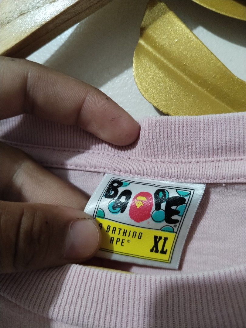 A Bathing Ape Pink T-Shirt XL (Category: Shirts) located in Manila. Submitted by bentong18188433 (Listing ID 1468617036, Image 2). Description: - Brand: A Bathing Ape (Bape) - Color: Pink - Design: Classic black ape head graphic with arched lettering on chest - Size: XL (collar tag attached) - Details: Signature small ape tag on the left sleeve - Fit: Regular fit, crewneck style - Condition: Excellent, ready to ship.