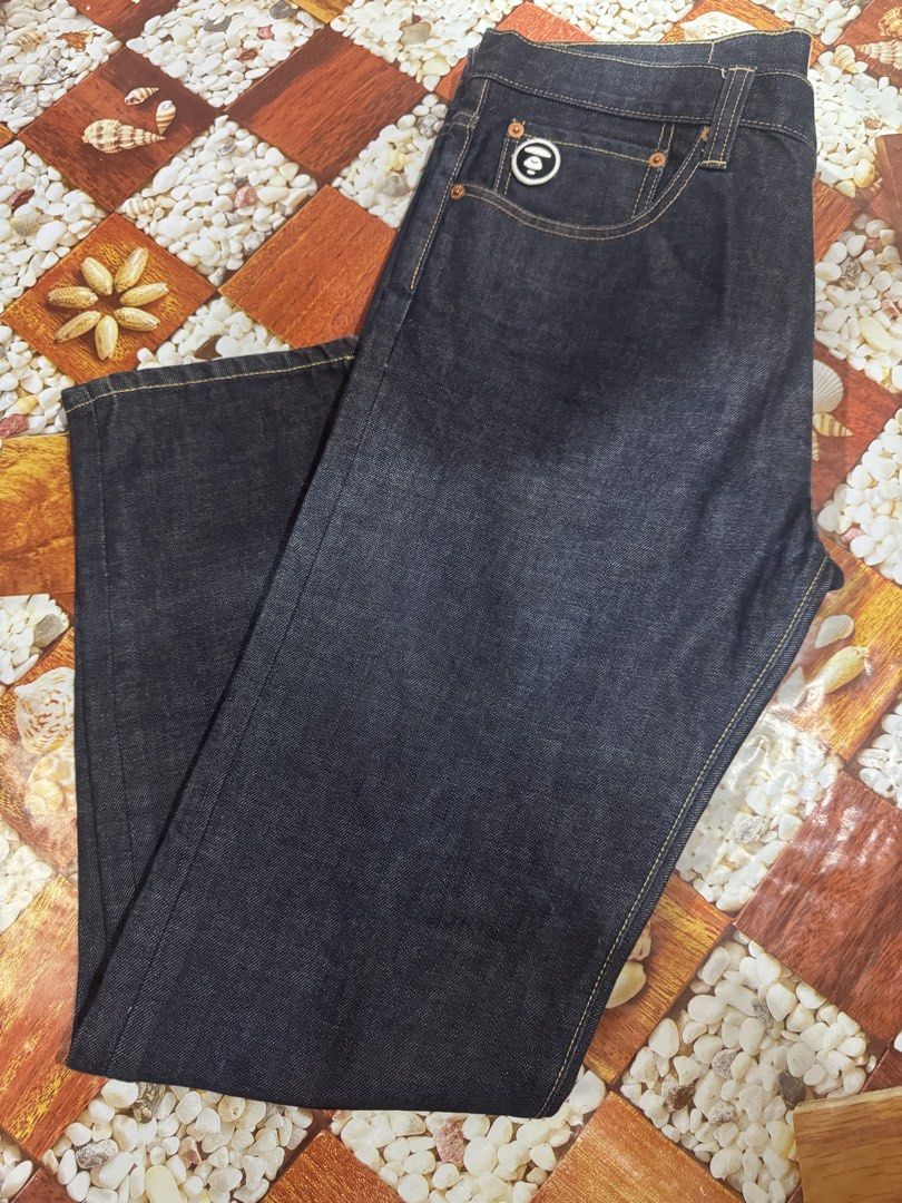 AAPE By A Bathing Ape Original 100% AAPE (Category: Luxury Apparel) located in Manila. Submitted by wildbear.e10374 (Listing ID 1468587003, Image 3). Description: - Brand: AAPE By A Bathing Ape - Item: Dark Denim Jeans - Size: W36 L31 - Fit: Regular fit with straight legs - Design: Big 'AAPE Now Union' graphic printed on the front leg - Details: Red back leather patch, red embroidered logo on the right back pocket, and branded AAPE buttons - Cond