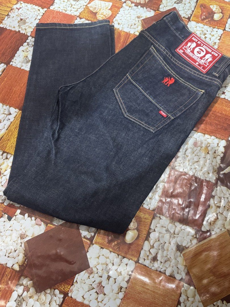 AAPE By A Bathing Ape Original 100% AAPE (Category: Luxury Apparel) located in Manila. Submitted by wildbear.e10374 (Listing ID 1468587003, Image 1). Description: - Brand: AAPE By A Bathing Ape - Item: Dark Denim Jeans - Size: W36 L31 - Fit: Regular fit with straight legs - Design: Big 'AAPE Now Union' graphic printed on the front leg - Details: Red back leather patch, red embroidered logo on the right back pocket, and branded AAPE buttons - Cond