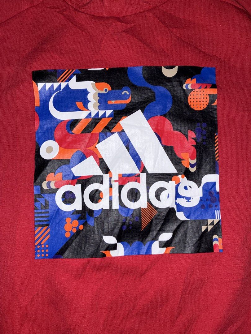 Adidas Red Dragon Graphic Sweatshirt (Category: Coats, Jackets and Outerwear) located in Placer. Submitted by talaalond61563 (Listing ID 1468711785, Image 3). Description: - Color: Bright red - Material: Comfortable, solid cotton for everyday wear - Front Design: Bold Chinese dragon art inside a square box with a white Adidas logo in the middle - Back Design: Small white Adidas logo near the collar - Hem Detail: Matching red patch near the bottom