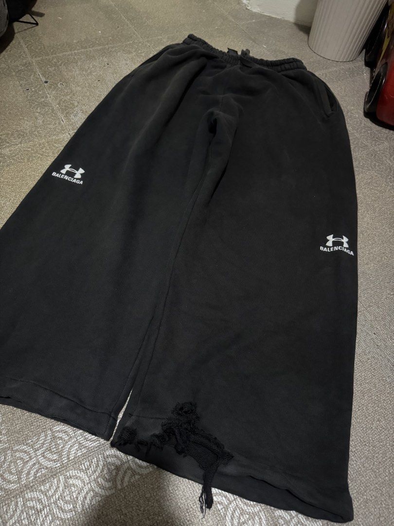 Balenciaga x Under Armour Sweatpants (Category: Joggers) located in Caloocan City. Submitted by eozilla (Listing ID 1468591680, Image 2). Description: - Brand: Balenciaga x Under Armour - Color: Black - Size: Large (L) - Fit: Wide leg with elastic waist and adjustable drawstring - Material: Premium cotton fleece, made in Portugal - Design: Under Armour logo prints and Balenciaga text on both lower legs - Details: Heavy distressing and raw hem on 